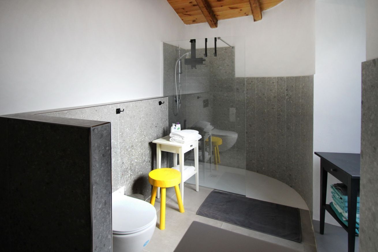 Een moderne badkamer met een douchecabine van glas, een witte wastafel en een gele kruk.