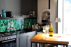 Eine Küche mit grüner Fliesenwand, einem Holztisch mit Weinflasche und Glas sowie diversen Küchenutensilien.