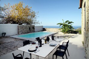 An outdoor dining area with a pool, stone walls, and a view of the sea.