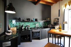 Uma cozinha moderna com armários escuros, painel de azulejos verdes e uma mesa de jantar de madeira com uma garrafa de vinho.