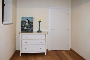 A hallway with a white dresser, a painting of a woman, a green candle holder, and a closed door.