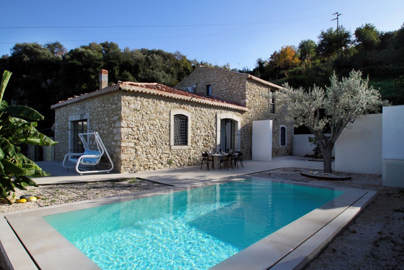 A stone house with a swimming pool, outdoor seating, and a tree.
