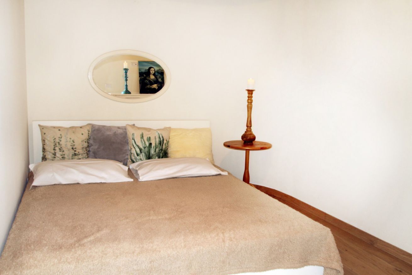 A neatly made bed with a beige blanket, two pillows, and a bedside table with a candle.