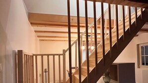 Een houten trap met een glazen afscheiding onderaan, die uitkomt op een plateau met een kleine tafel en een vaas.