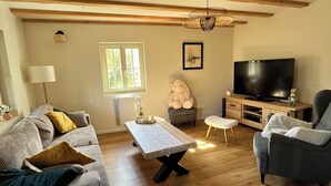 Een woonkamer met een bank, fauteuil, salontafel, televisie en een raam.