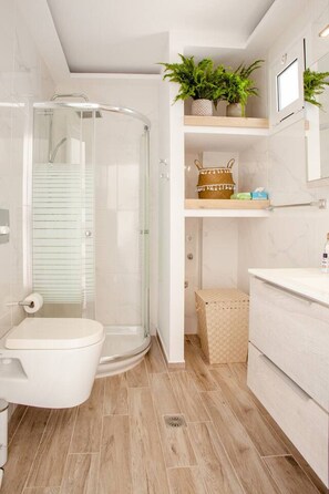 Ein modernes Badezimmer mit einer Glaskabine zur Dusche, Toilette, Waschbecken und Ablagefläche mit Pflanzen und einem Korb.