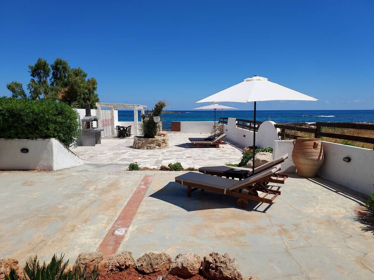 A rooftop patio with lounge chairs, a white umbrella, and a view of the ocean.