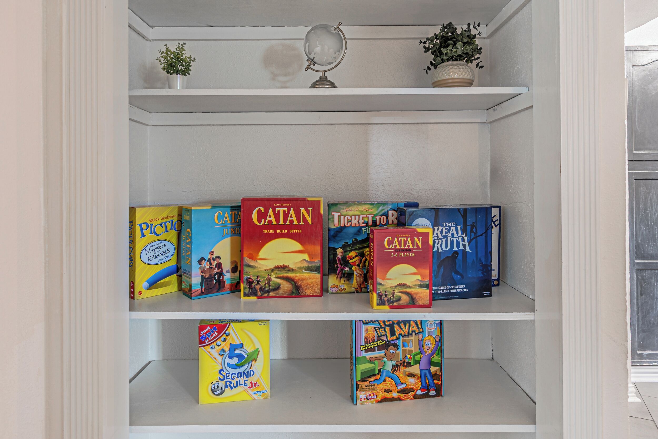 A shelf with board games including Catan, Ticket to Ride, and The Real Truth.