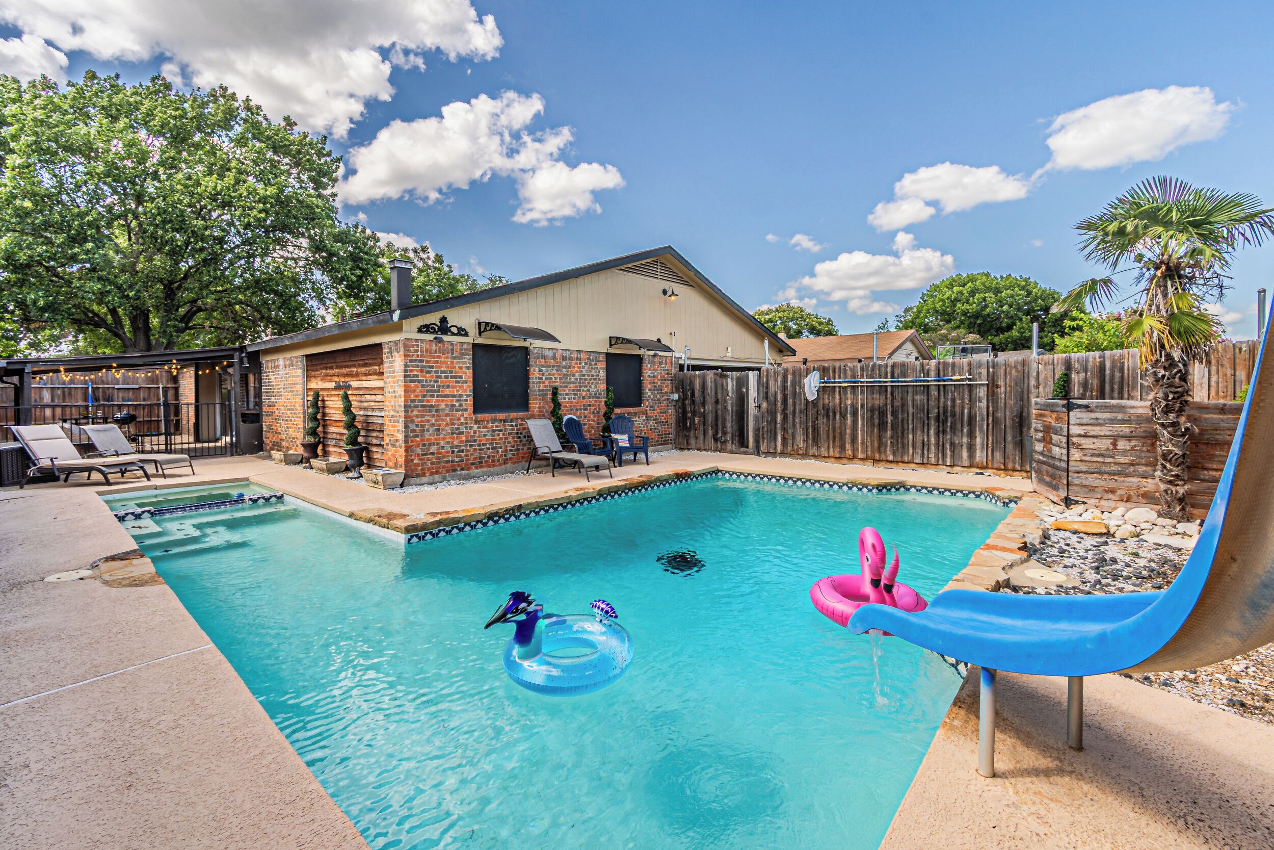 A backyard with a swimming pool, a slide, and a brick house.
