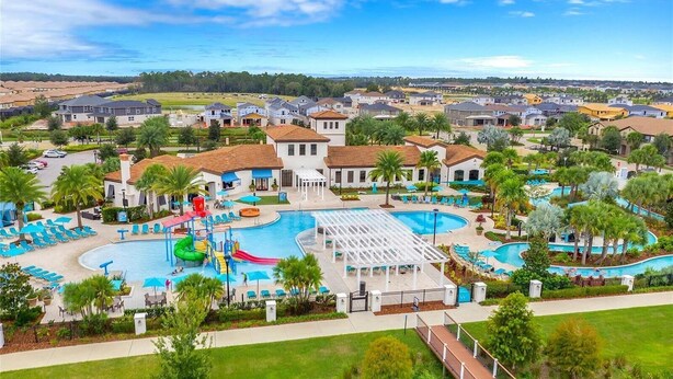 A residential area with a large swimming pool, multiple houses, and a well-maintained lawn. - Lakefront 5BR Villa • Private Pool near Disney (Kissimmee)