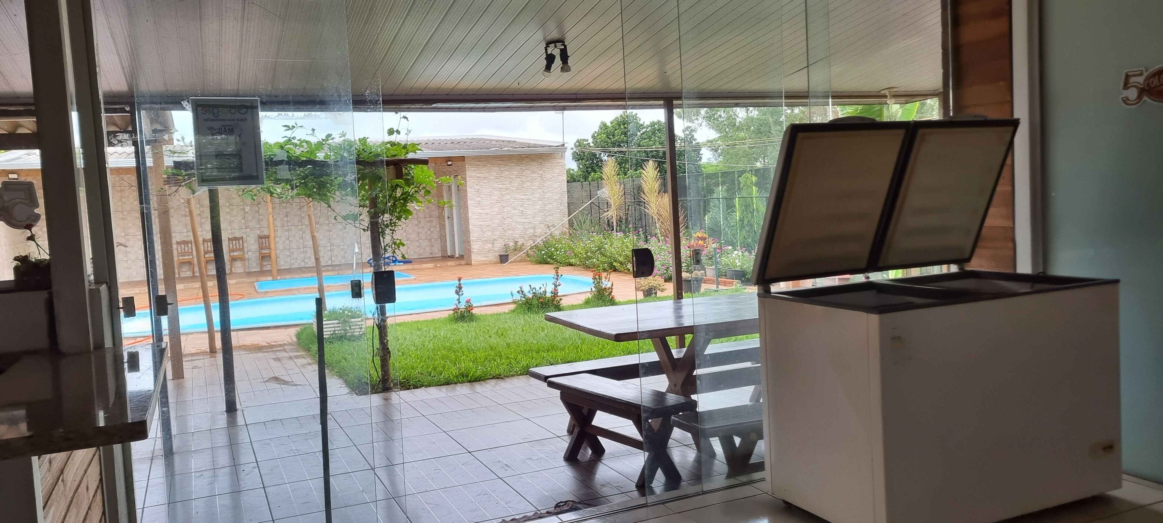 A room with a glass door leading to a patio with a pool, a table, and a speaker.