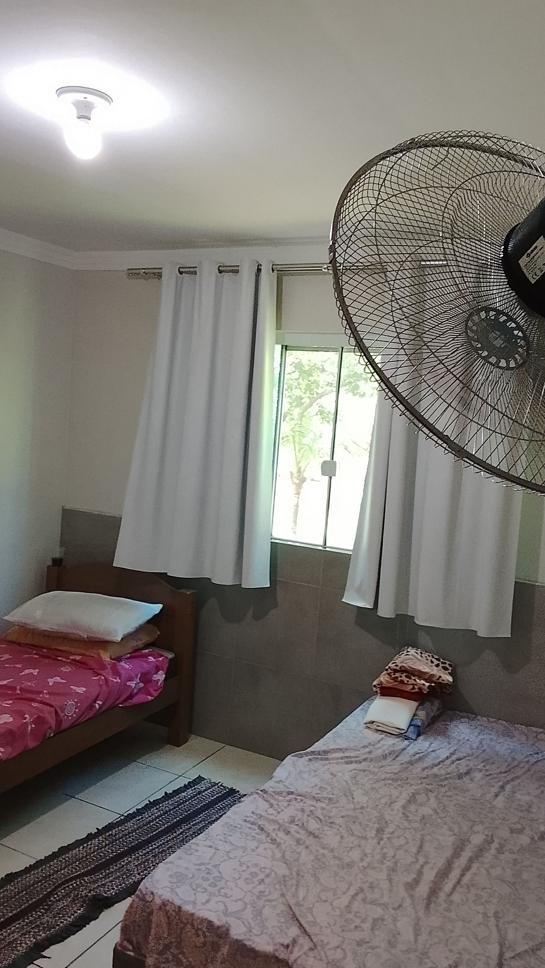 A room with two beds, a ceiling fan, a window with curtains, and a visible door.
