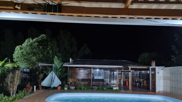 Una piscina amb zona coberta, envoltada per un jardí i un edifici amb teulada emblenquinada.
