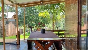Terrassa exterior amb taula i bancs de fusta, envoltada per parets de vidre i una zona coberta.