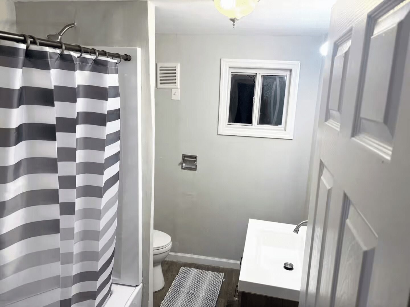 Une salle de bain avec un rideau de douche à rayures, des toilettes, une fenêtre et un lavabo.