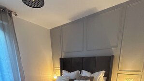 Ein ordentlich bezogenes Bett mit Kissen und Decke, eine Nachttischlampe und eine Wandleuchte.