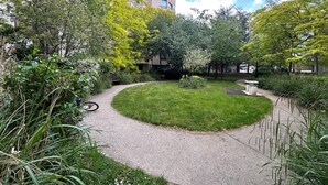 Ein begrüntes Innenhof mit einem gewundenen Pfad, einem kleinen Rundgarten und einem Gebäude im Hintergrund.