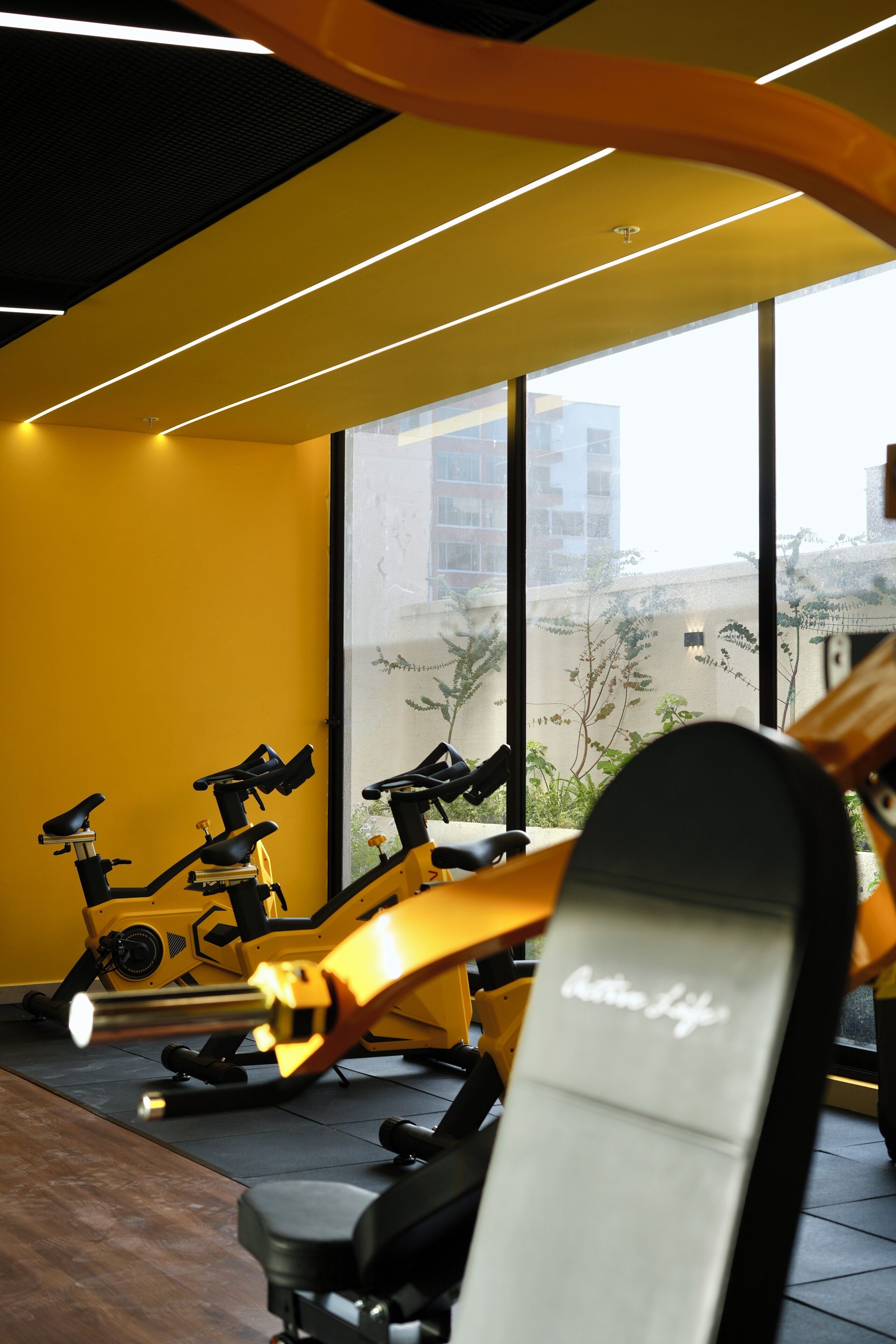 A gym with exercise equipment, large windows, and a yellow wall.