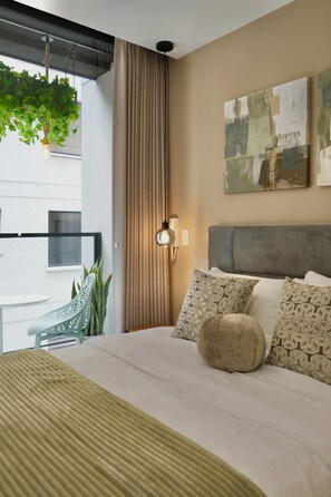 Ein Hotelzimmer mit Bett, einer hängenden Pflanze, Blick ins Freie und einem Bild an der Wand.