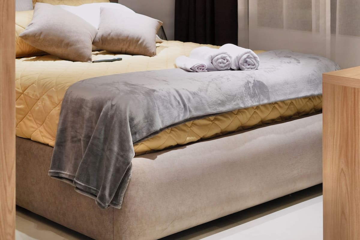 A modern bedroom with a tufted headboard, a bed with a quilted cover, a bedside table, and a wall-mounted phone.