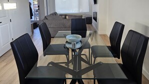 Uma sala de estar moderna com uma mesa de jantar de vidro, rodeada por cadeiras pretas, um sofá e uma janela grande.