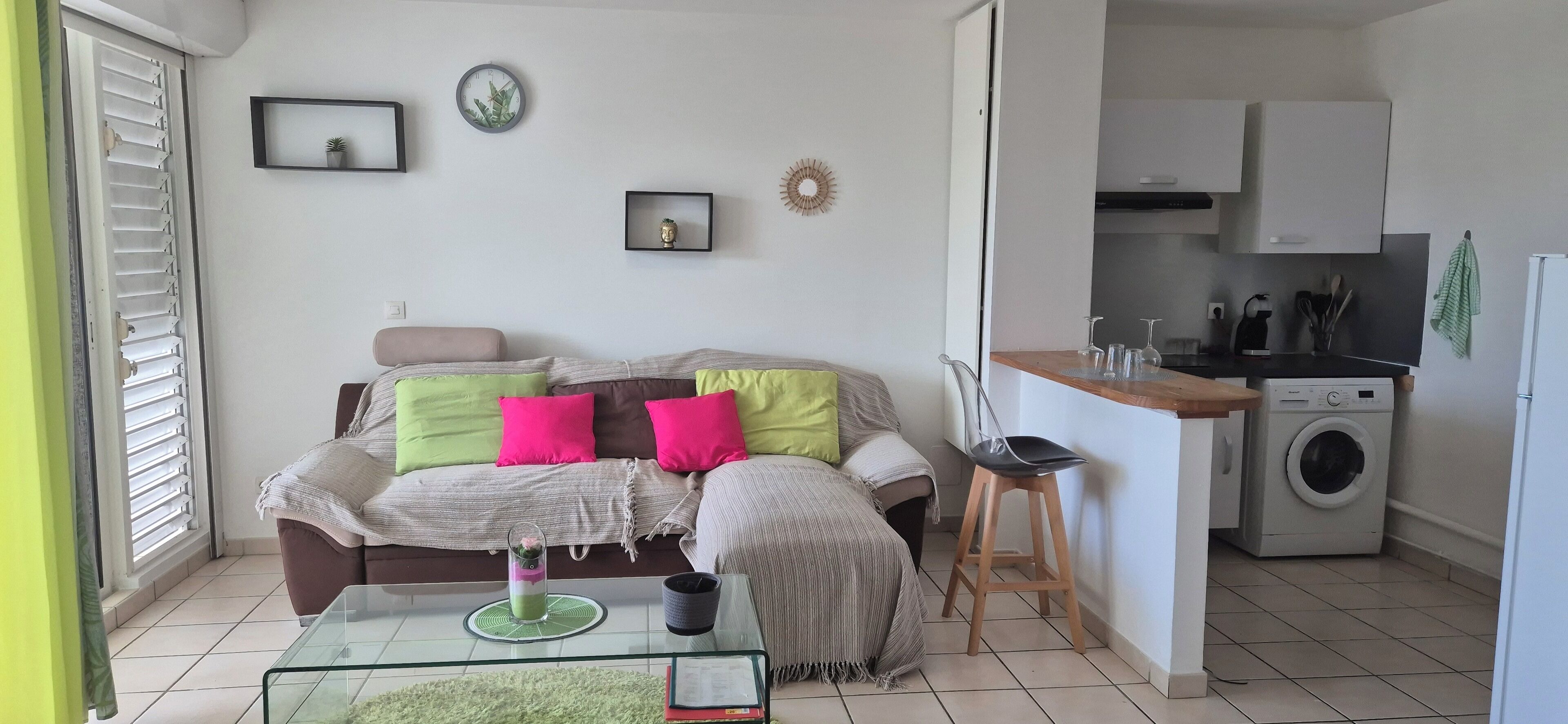 Un espacio habitable compacto con sofá, mesa de centro y una pequeña cocina que incluye lavadora.