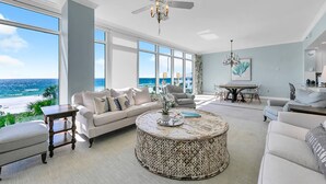 A spacious living room with a large window overlooking the ocean, a round coffee table, and a modern ceiling fan. - Sterling Reef 301 (Panama City Beach)