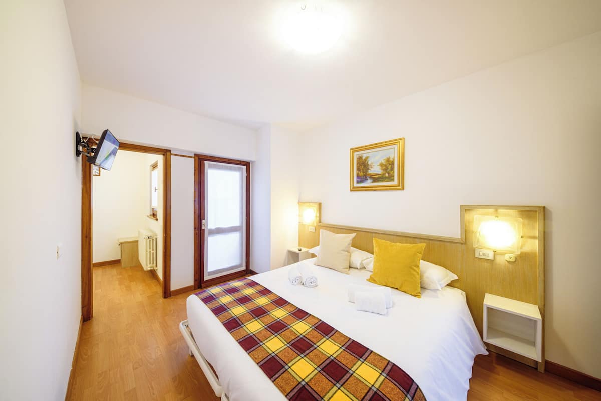 A hotel room with a bed, a nightstand, a wall-mounted lamp, a door, and a painting.