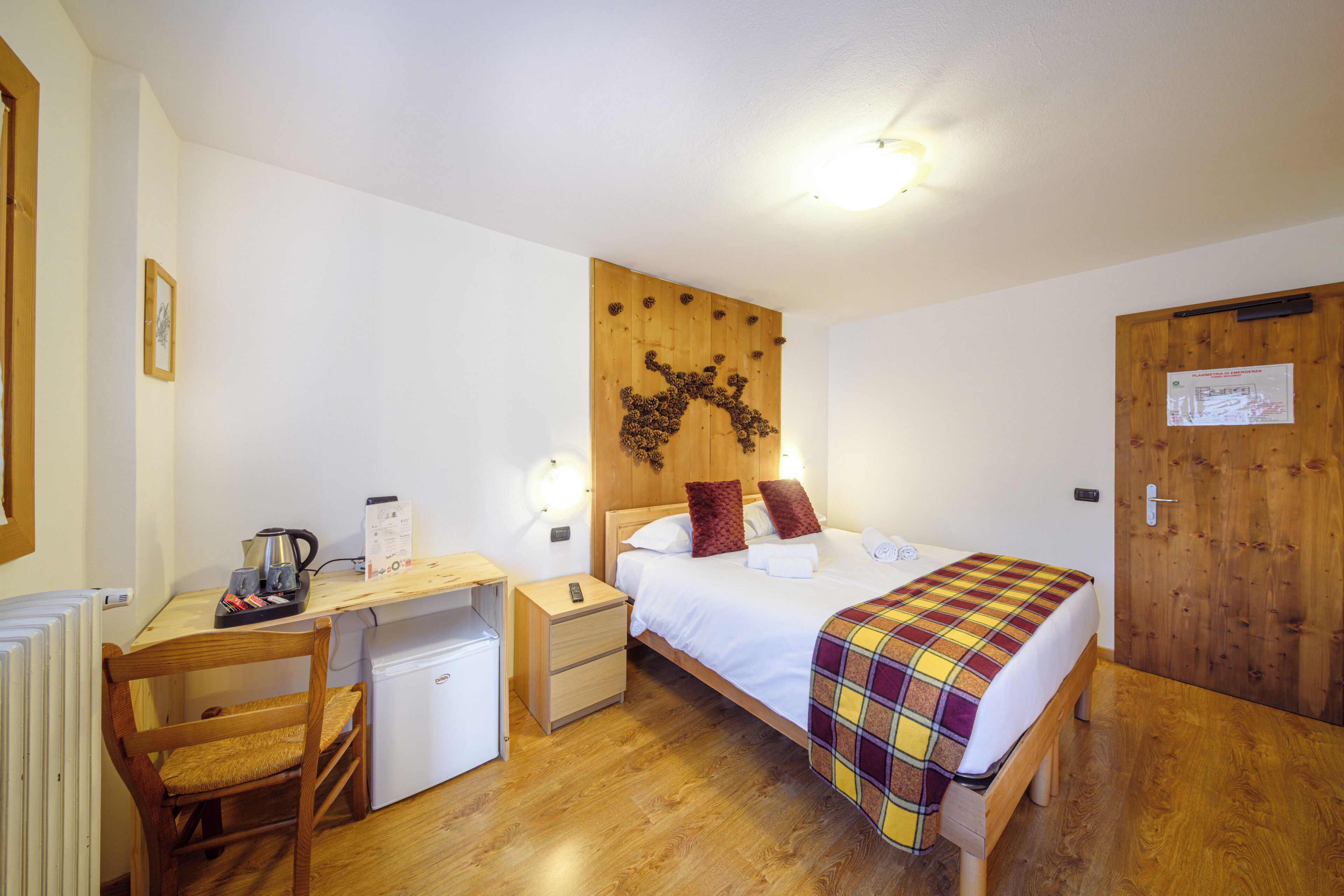 Una habitación pequeña y ordenada con una cama, un escritorio, una silla, un refrigerador pequeño y una puerta de madera.