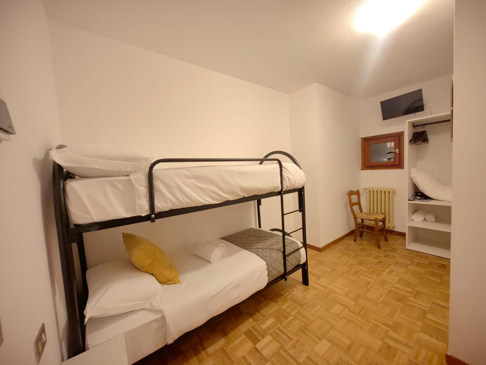 A bunk bed room with a wooden floor, a chair, a radiator, and a TV on the wall.
