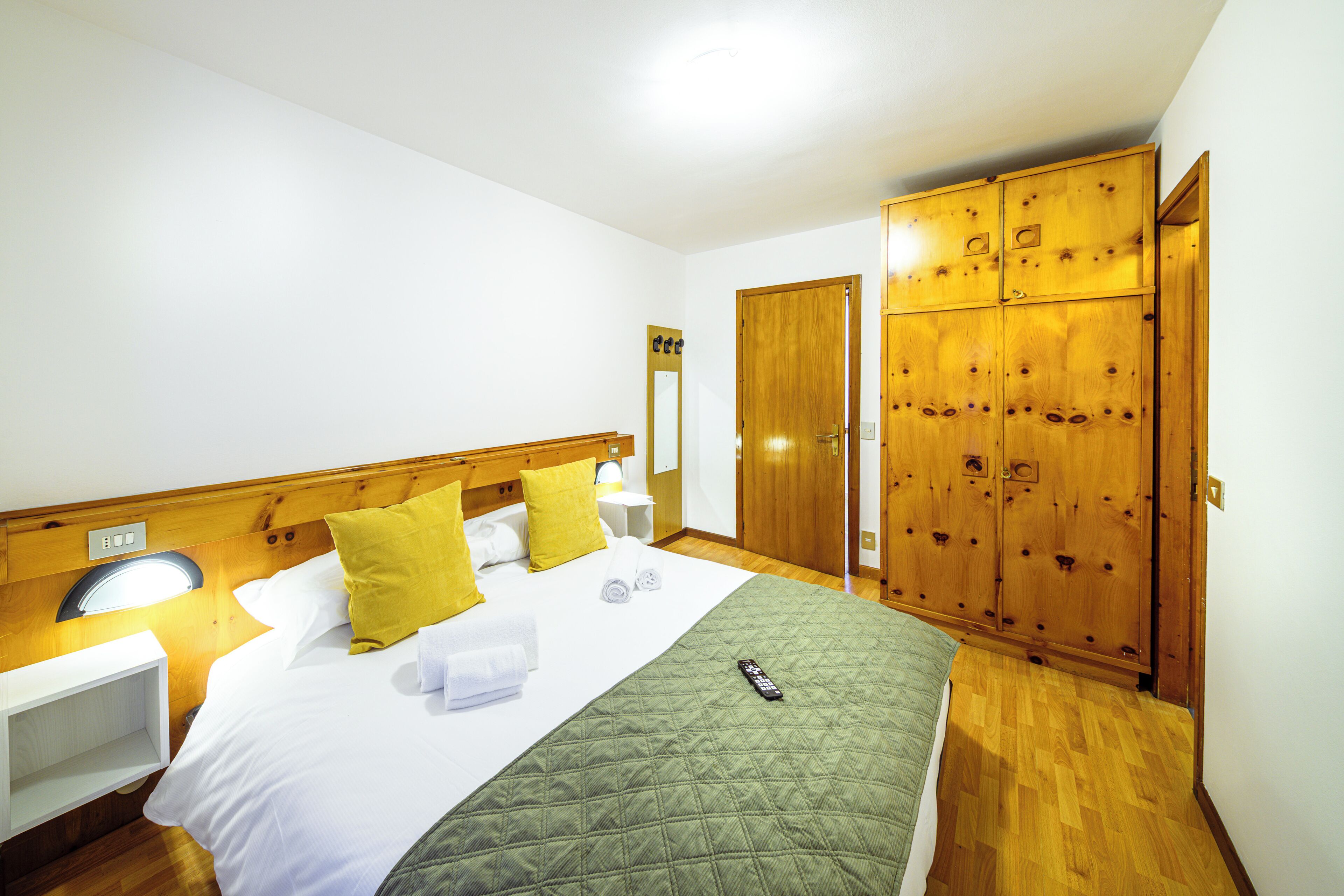 A hotel room with a bed, a nightstand, a mirror, a wardrobe, and a wooden headboard.