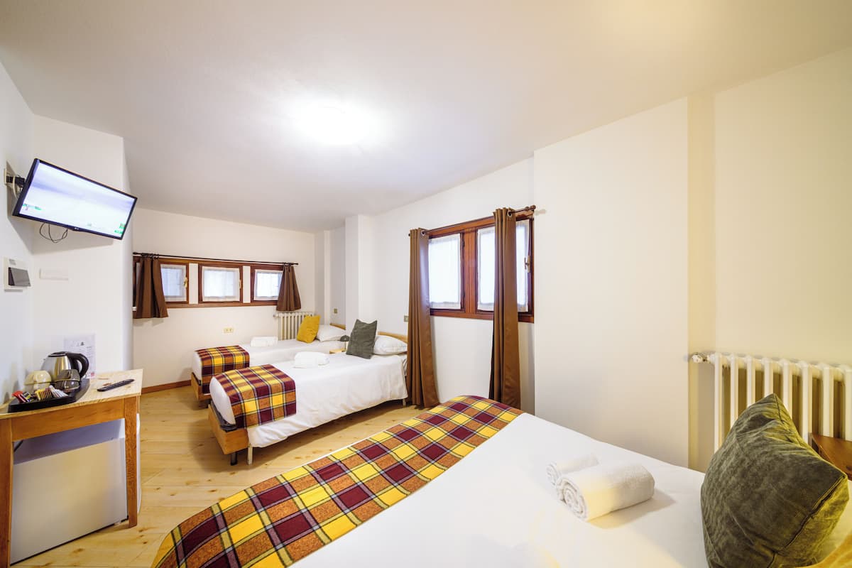 A hotel room with two beds, a desk, a television, and a window with curtains.