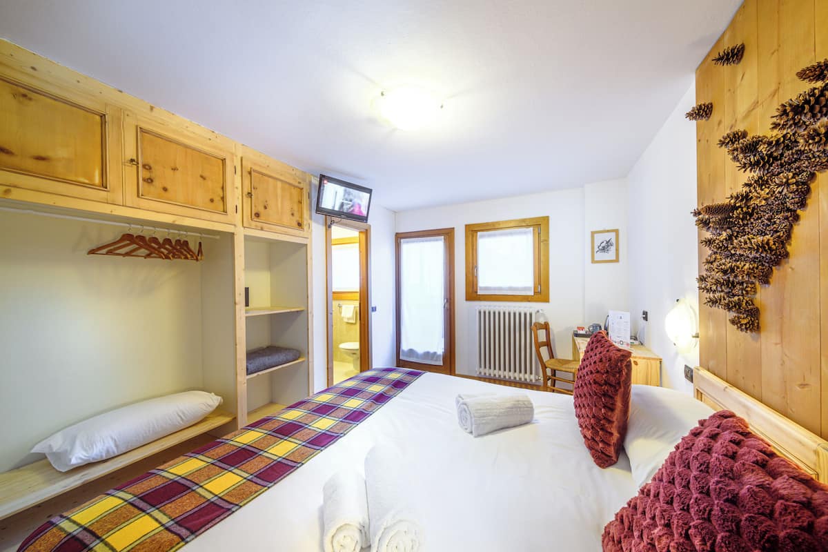 A bedroom with a bed, a wooden wardrobe, a television, and a pine cone decoration.