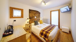 A bedroom with a wooden bed, a desk with a kettle, a chair, and a television mounted on the wall. - Hotel Ambassador Bormio (Bormio)