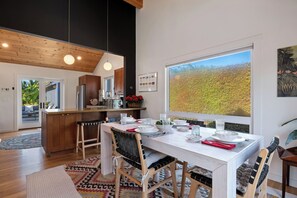 Eine moderne Küche mit Holzausstattung, ein Essbereich mit großem Fenster und Blick auf einen Wald.