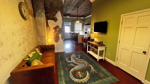 Una sala de estar con un sofá marrón, un tapete verde con diseño de dragón, una cocina al fondo y un televisor montado en la pared.