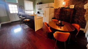 Una cocina con una isla central, taburetes de bar, una mesa de comedor con sillas y una pared de ladrillo.