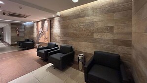 A lobby with a modern design, featuring a stone wall and several black leather chairs. - Flat com Piscina Academia e Sauna em Guas Claras (Águas Claras)