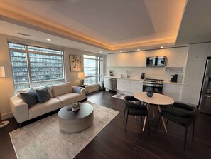 A modern living room with a sofa, coffee table, and dining area. - Waterfront 1 BR corner unit - 6 appliances & gym (Halifax)
