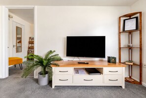 A room with a flat-screen TV on a wooden stand, a white cabinet with drawers, a potted plant, and a shelf with a framed certificate.