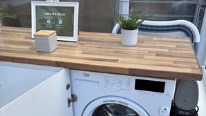 Een compacte wasmachine met een bedieningspaneel, een klein potplantje en een lijst met een bord op een houten aanrecht.