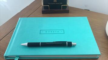 A teal notebook with a pen on top, labeled 'GUESTS,' and a black box with 'The Garden Annex 306' on a wooden table.