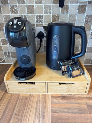 Une machine à café, une bouilloire et des paquets de biscuits sur un plateau en bois.