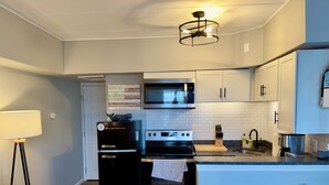 Uma cozinha moderna com geladeira preta, fogão de aço inoxidável e micro-ondas. Há uma tábua de corte de madeira e um porta-facas no balcão.