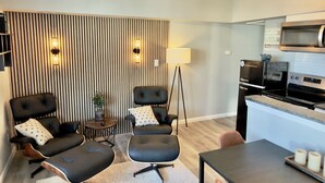 Uma sala de estar moderna com um conjunto de sofá, uma mesa de centro e uma mesa de jantar. Há uma cozinha com micro-ondas e fogão.