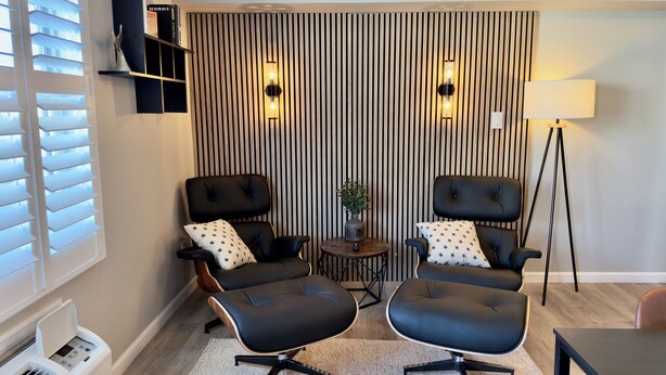 Uma sala de estar moderna com duas poltronas de couro preto, uma mesinha de apoio com uma planta e um abajur.