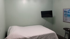 A room with a bed, a mounted TV, and a window with a beach view.
