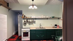 A compact kitchen with a stove, sink, and hanging pots. There are shelves above the counter holding various kitchen items.