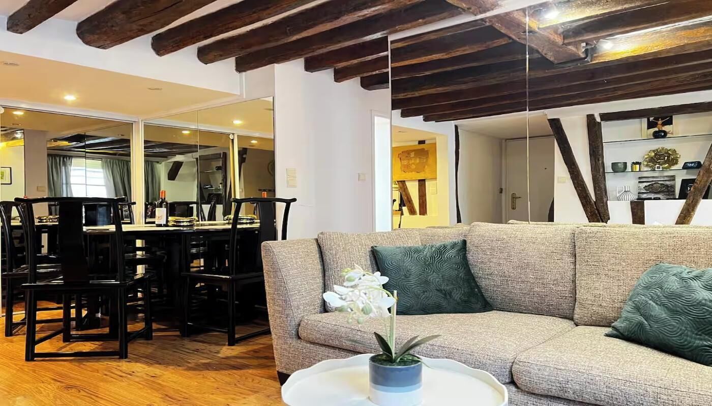 A living room with a sofa, a dining table with chairs, and a kitchen area visible through an open door.