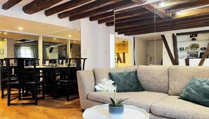 Un salon avec un canapé, une table à manger entourée de chaises et un coin cuisine visible à travers une porte ouverte.